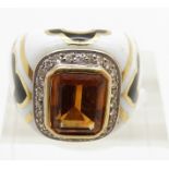 A yellow metal ring set with an emerald cut citrine surrounded by diamonds set with black and