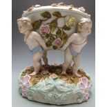 German figural porcelain oil lamp supported by four putti and decorated with applied flowers, blue