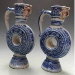 A pair of German Mettlach style mask spouted pedestal ewers of circular form, H20cm