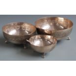 Set of three graduated white metal bowls with embossed decoration, raised on three feet and marked