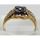 A yellow metal ring set with four round cut sapphires and diamonds in a flower cluster, 3.3g, size