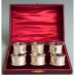 Cased set of six Edward VII hallmarked silver napkin rings, with engraved foliate decoration and