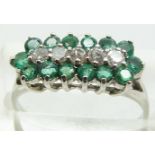A 9ct white gold ring set with a row of diamonds surrounded by emeralds, 2.1g, size L