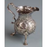 Georgian hallmarked silver cream jug with embossed decoration and raised on three feet, London