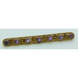 A yellow metal early 20thC brooch set with alternating amethysts and gold flowers, 4.4g, 6.2cm long
