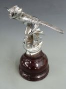 Winged nymph riding a winged wheel vintage car mascot, on turned wooden base, overall height 20.5cm