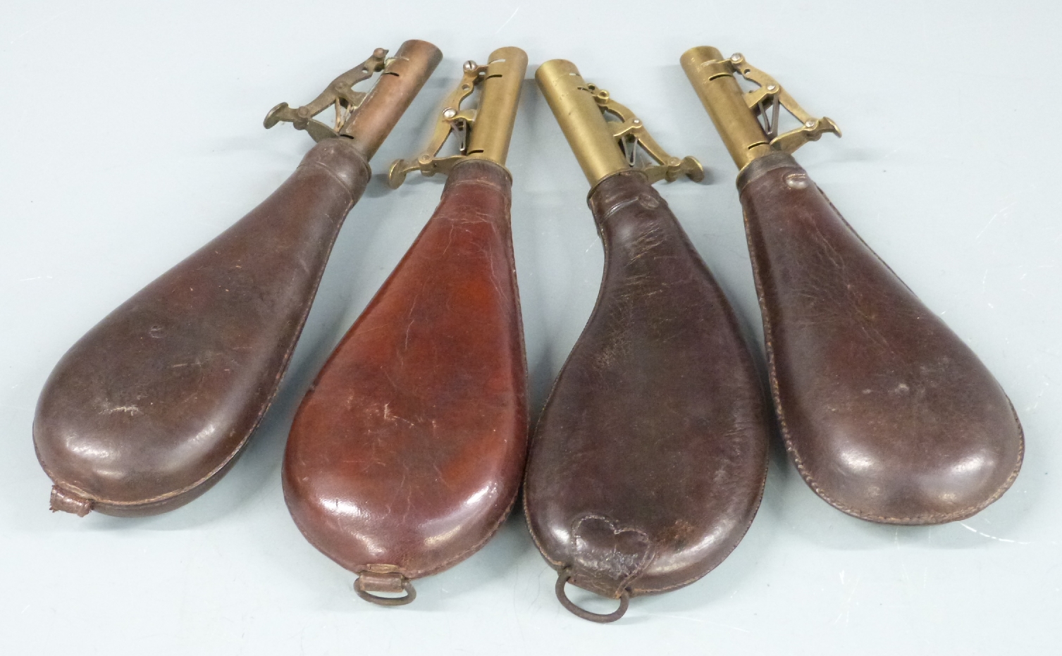 Four leather and brass shot flasks, one kidney shaped and two with belt loops, largest 22.5cm long.