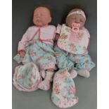Two silicone dolls both with closed mouths and eyes, brown hair and soft bodies, one marked to the