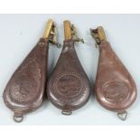 Three leather and brass shot flasks, both with embossed shooting scenes to both sides and belt