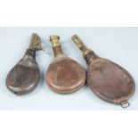 Three leather and brass shot flasks, largest 24.5cm long.