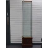 A glazed cabinet with three glass shelves raised on a wooden base with lockable storage compartment,