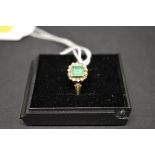 An antique unmarked gold ring set central emerald surrounded by diamond chips, and diamond chip