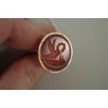 An unmarked yellow metal oval intaglio carved carnelian seal, depicting a Pelican feeding young.