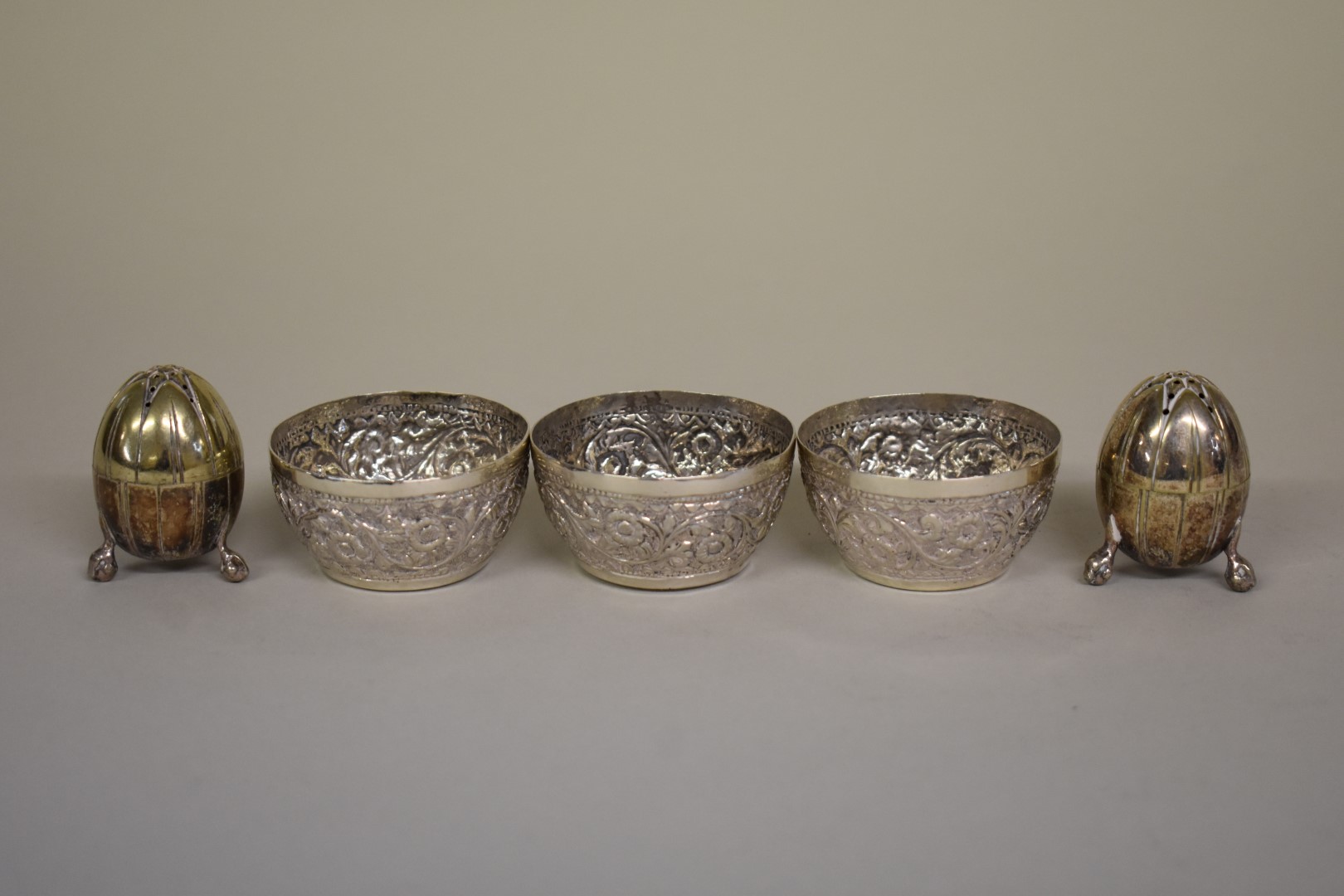 Three Arabic floral chased white metal salts; together with a pair of metal pepperettes.