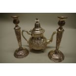 An Indian white metal teapot; together with a pair of similar candlesticks.