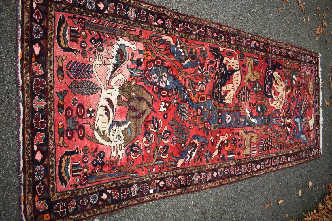 An Eastern rug, having animal motifs on a red field, with floral borders, 320 x 127cm.