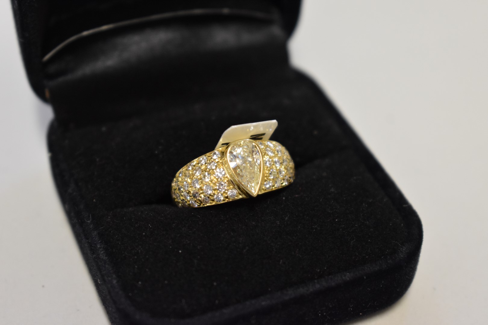 A pear cut diamond gold ring, hallmarked 750, the central diamond 0.67ct and pave set shoulders 0.