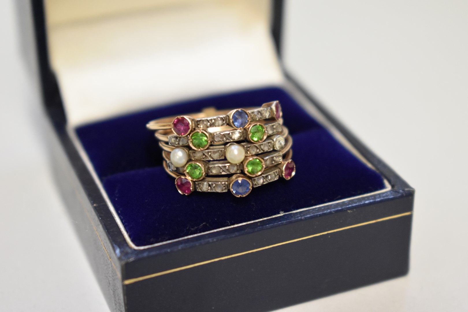 A five strand gem set unmarked yellow metal ring, studded sapphires, rubies, peridots, diamonds