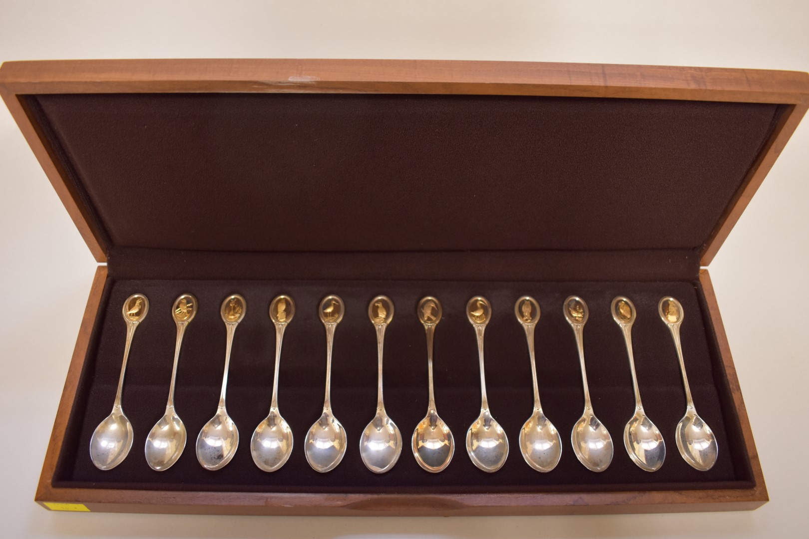 A cased set of twelve RSPB silver and gold tea spoons, by John Pinches, London 1975, 322g, with