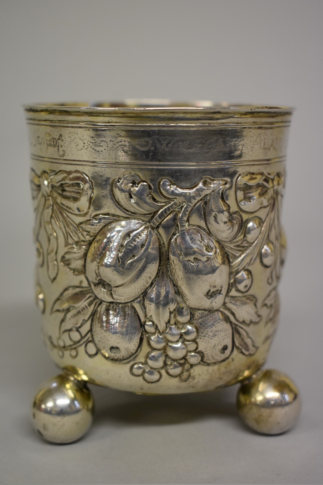 An antique Continental white metal beaker, having floral fruit and ribbon chased decoration,