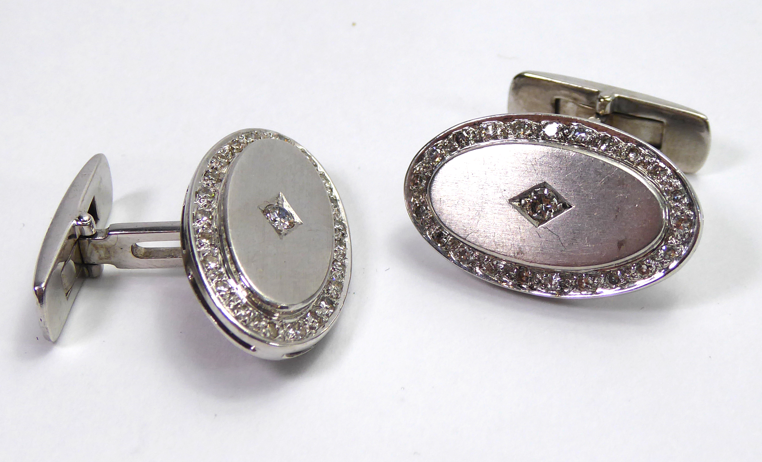 A PAIR OF OVAL FORM WHITE METAL AND DIAMOND CUFFLINKS. (16.9g