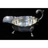 AN EARLY 20TH CENTURY SILVER SAUCE BOAT Having a scalloped edge with scrolled triform legs,