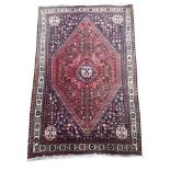 A PERSIAN SHIRAZ WOOLLEN RUG Having a lozenge design to central field on red ground with floral