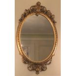 A 19TH CENTURY OVAL GILT FRAMED MIRROR Crested with a ribbon entwined floral cartouche. (67cm x