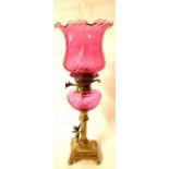 A VICTORIAN CRANBERRY GLASS AND BRASS OIL LAMP Figured with a winged cherub. (63cm)