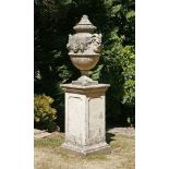 A composition stone urn, cover and pedestal,the baluster shaped urn cast with masks and fruiting