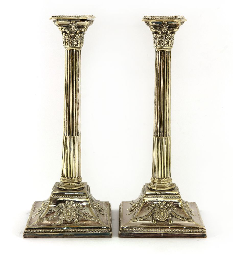 A pair of silver-plated Corinthian column candlesticks,terminating in sloping square bases,