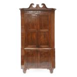 A George III mahogany standing corner cupboard,having a scrolled cornice over four panelled doors