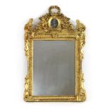 A carved giltwood wall mirror,late 19th/early 20th century, the shaped crest with ribbon-tied