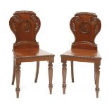 A pair of George IV mahogany hall chairs, the cartouche-shaped backs having carved, scrolled and
