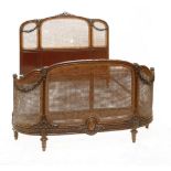 A French walnut double bed, with carved decoration, a caned headboard and double-caned footboard,