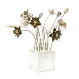 A silver painted group of metal flowers of varying designs and heights, arranged on a concrete cube,