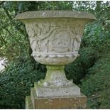 A pair of composition stone urns, the sides moulded with trailing vines, on pedestal bases, 62cm