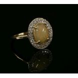 A gold opal cabochon and diamond cluster ring, an oval cabochon opal claw set to a border of