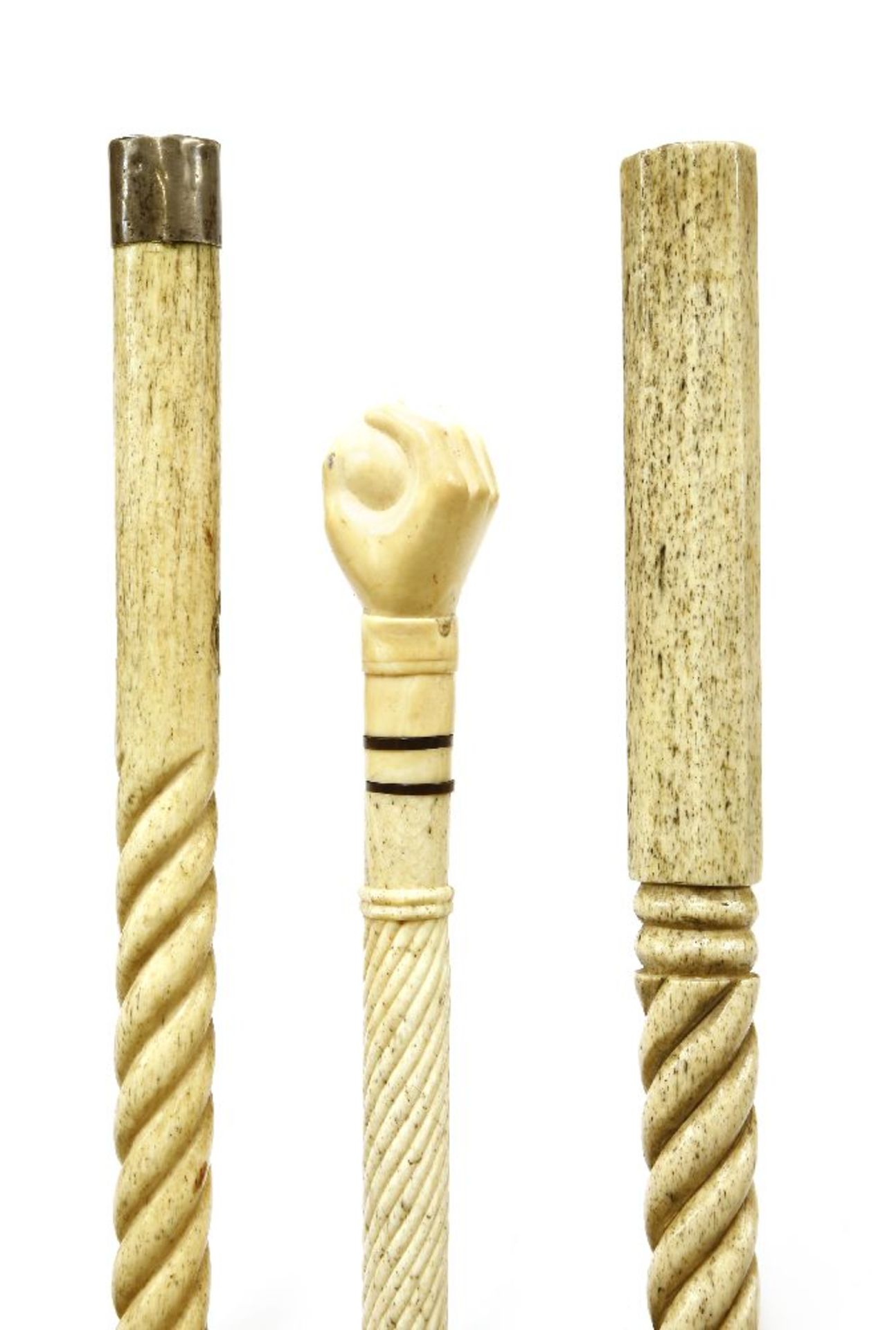 Three marine ivory and whalebone walking sticks,the first with a carved hand gripping a ball, with