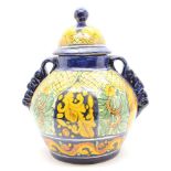 A Mexican Majolica jar and cover, with yellow arched decoration, height 37cm, raised on mahogany