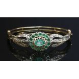 An emerald and diamond cluster hinged bangle, with an oval mixed cut emerald and circular mixed