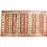 A Kilim rug with stylised geometric designs on a white ground within a red border, together with a