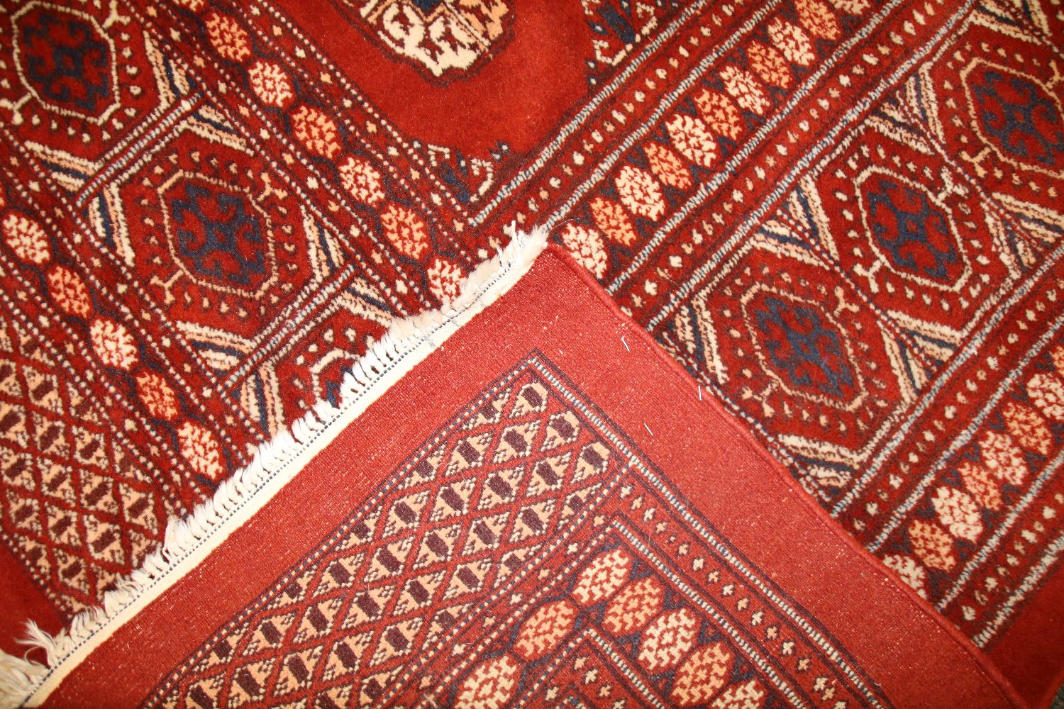 A Persian Bokhara carpet, the brick red fields with repeating elephant's foot motifs within a - Image 2 of 2