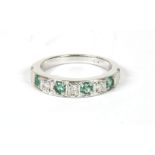 A white gold diamond and emerald half eternity ring, four round cut diamonds between three brilliant