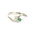 A white gold two stone emerald and diamond crossover ring, stamped 750, tested as approximately 18ct