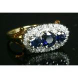 An 18ct gold three stone sapphire and diamond, landscape, oval cluster ring