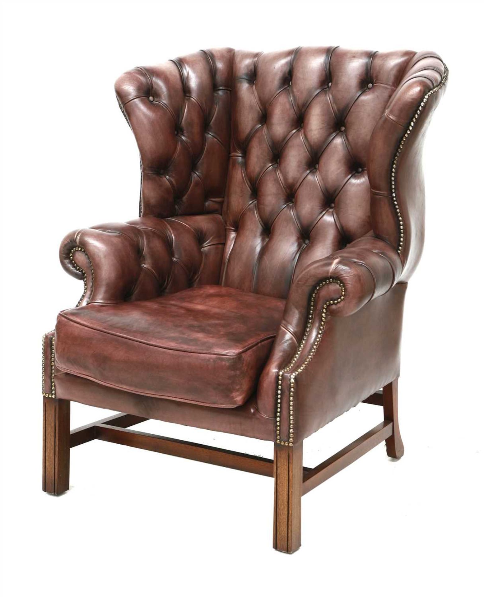 A deep buttoned brown leather wing armchair,
