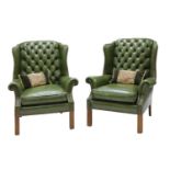 A pair of green leather wing armchairs,