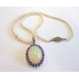 A white gold pendant set with a large cabouchon opal and surrounding amethysts on a single-strand