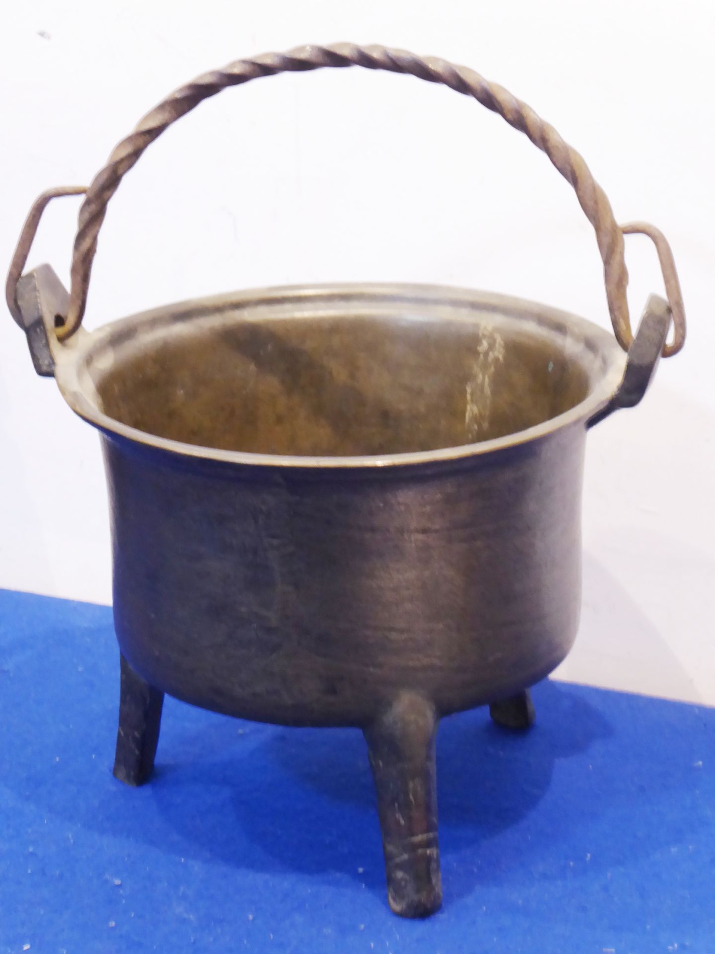 A 17th century bronze cooking pot with wrythern iron handle and raised on three tapering triangular